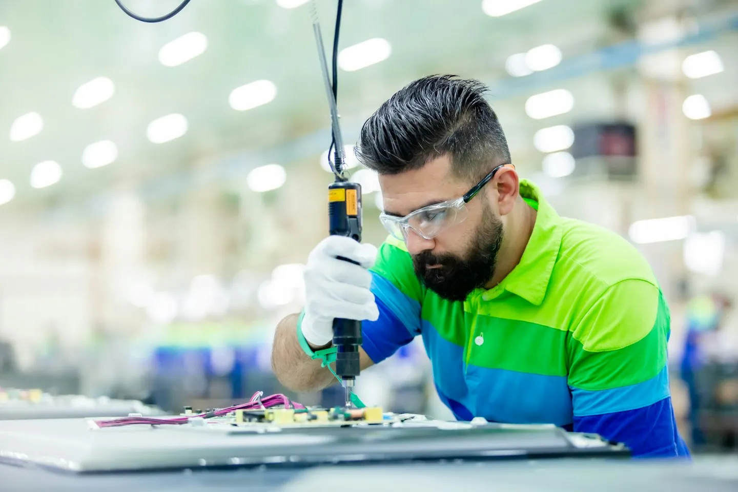 Technician wearing safety glasses and using a handheld tool at an assembly workstation