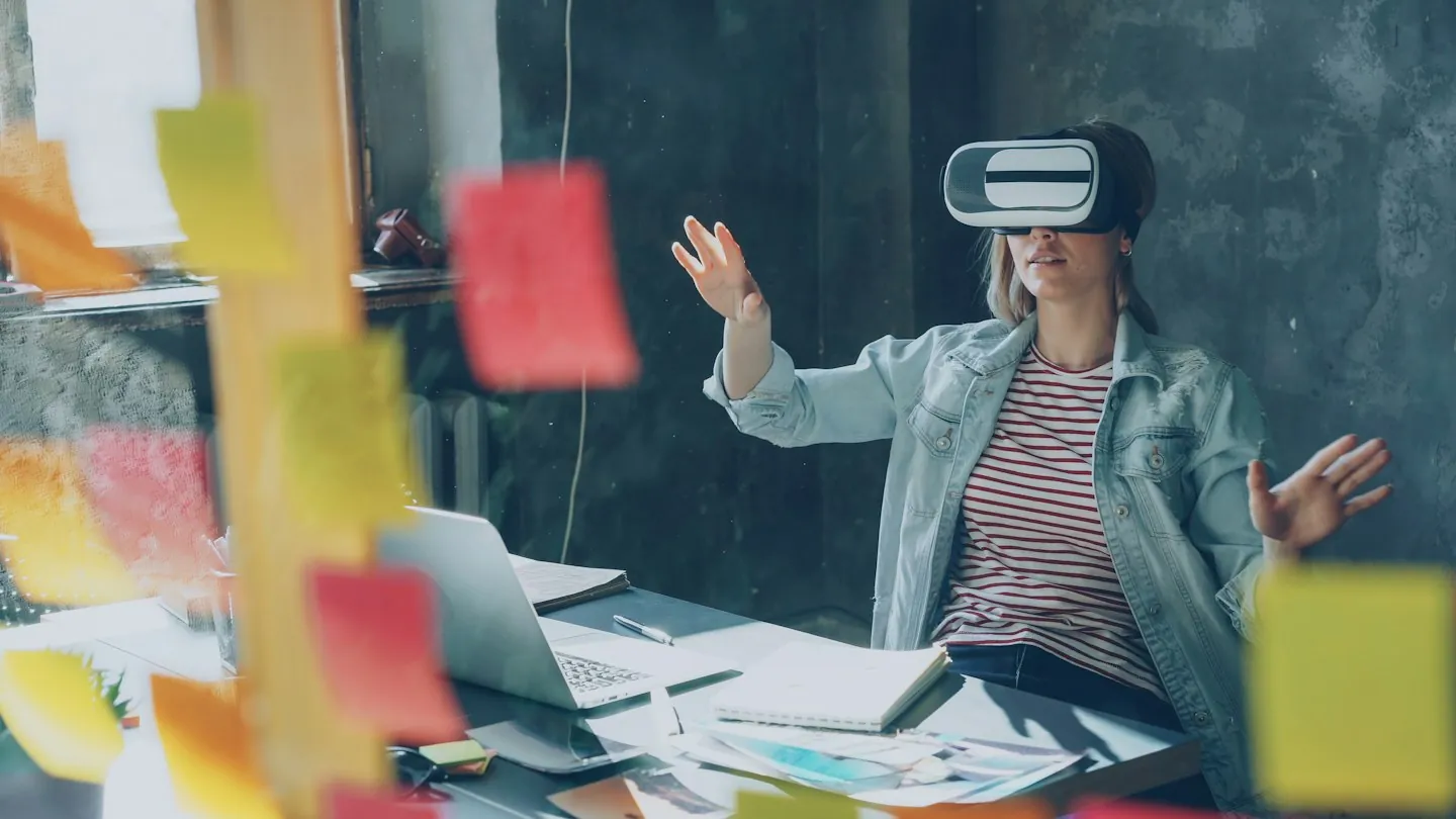 Woman seated at a desk using a virtual reality headset with her hands raised